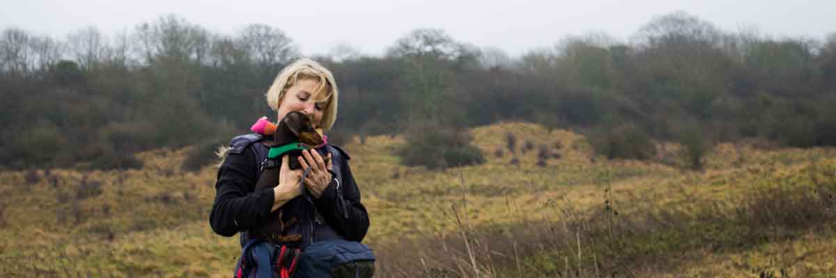 Miranda carrying a daschund puppy in a field.
